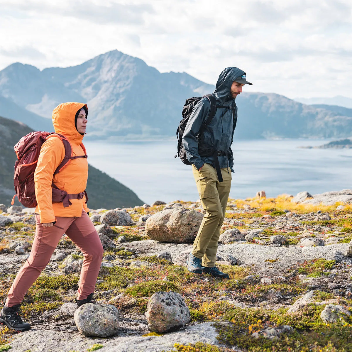 Woman hiking in orange Helly Hansen Womans Loke 2.0 Waterproof Jacket, showcasing its performance in outdoor mountain terrain.