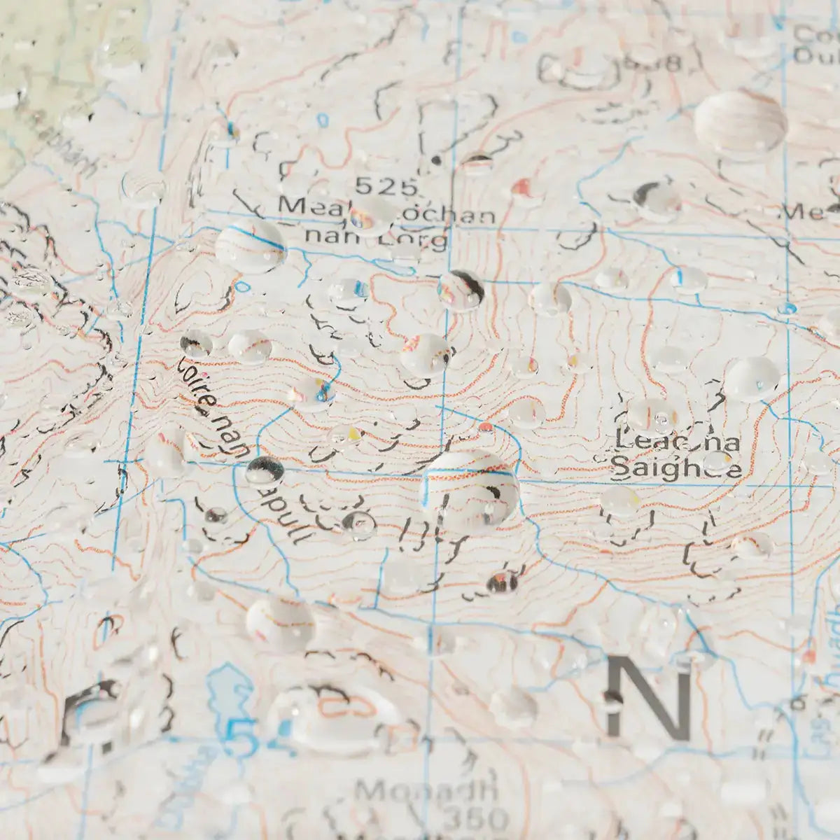 Close-up of topographic map inside Highlander Wanderer map case with water droplets, showing detailed terrain and contour lines for hillwalking