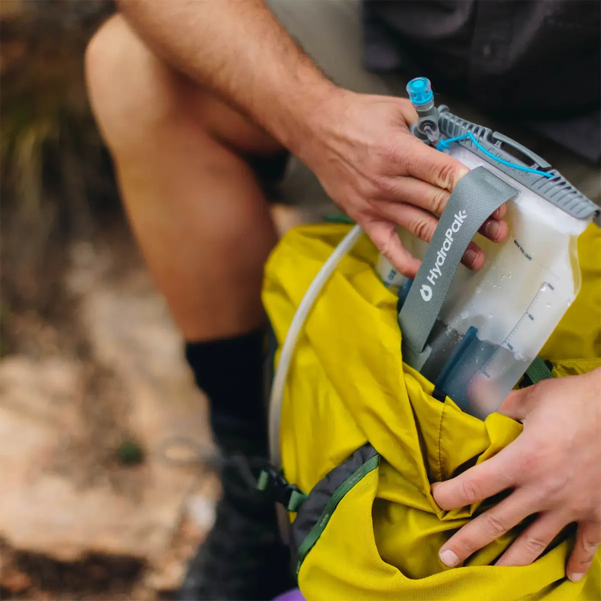 Close-up of HydraPak Contour Clear Water Reservoir being packed into a yellow hiking bag, emphasizing ease of use and outdoor readiness.