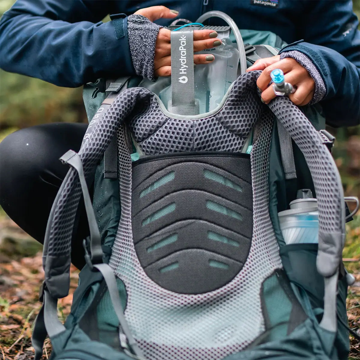 HydraPak Contour Clear Water Reservoir being inserted into a backpack, highlighting its ergonomic fit and hydration tube accessibility.