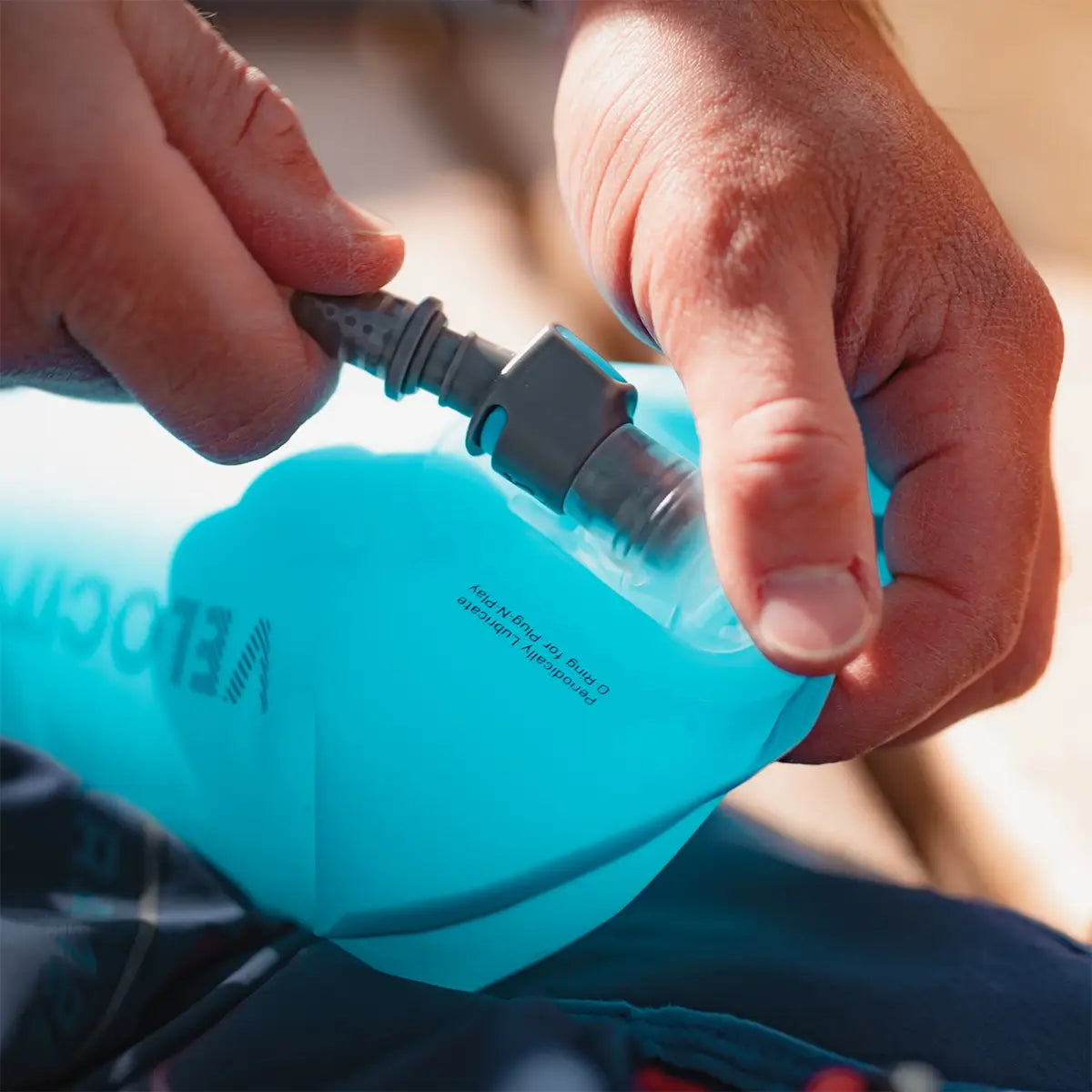 Close-up of hands connecting the hose to the HydraPak Velocity Hydration Water Reservoir, highlighting its secure and leak-proof valve system.