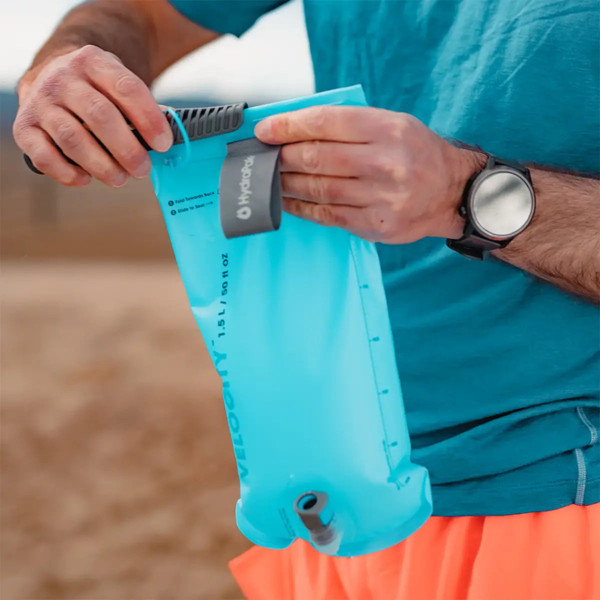 Man opening the HydraPak Velocity Hydration Water Reservoir, demonstrating its wide top opening for easy filling and cleaning during outdoor use.