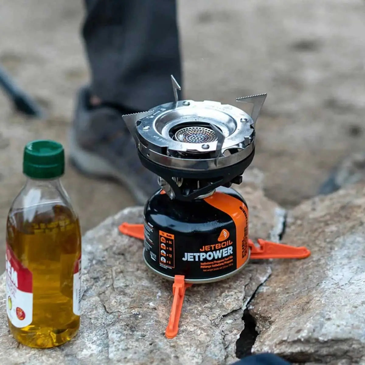 Jetboil Jetpower fuel canister with burner setup on rocky terrain, part of the Jetboil Sumo Carbon Cooking System. Reliable for outdoor use.
