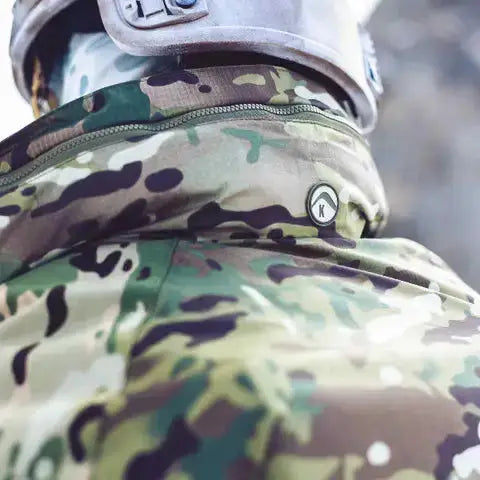 Close-up of a Keela Mk5 winter jacket with a high collar and a small circular logo patch, worn by a person in an outdoor setting.