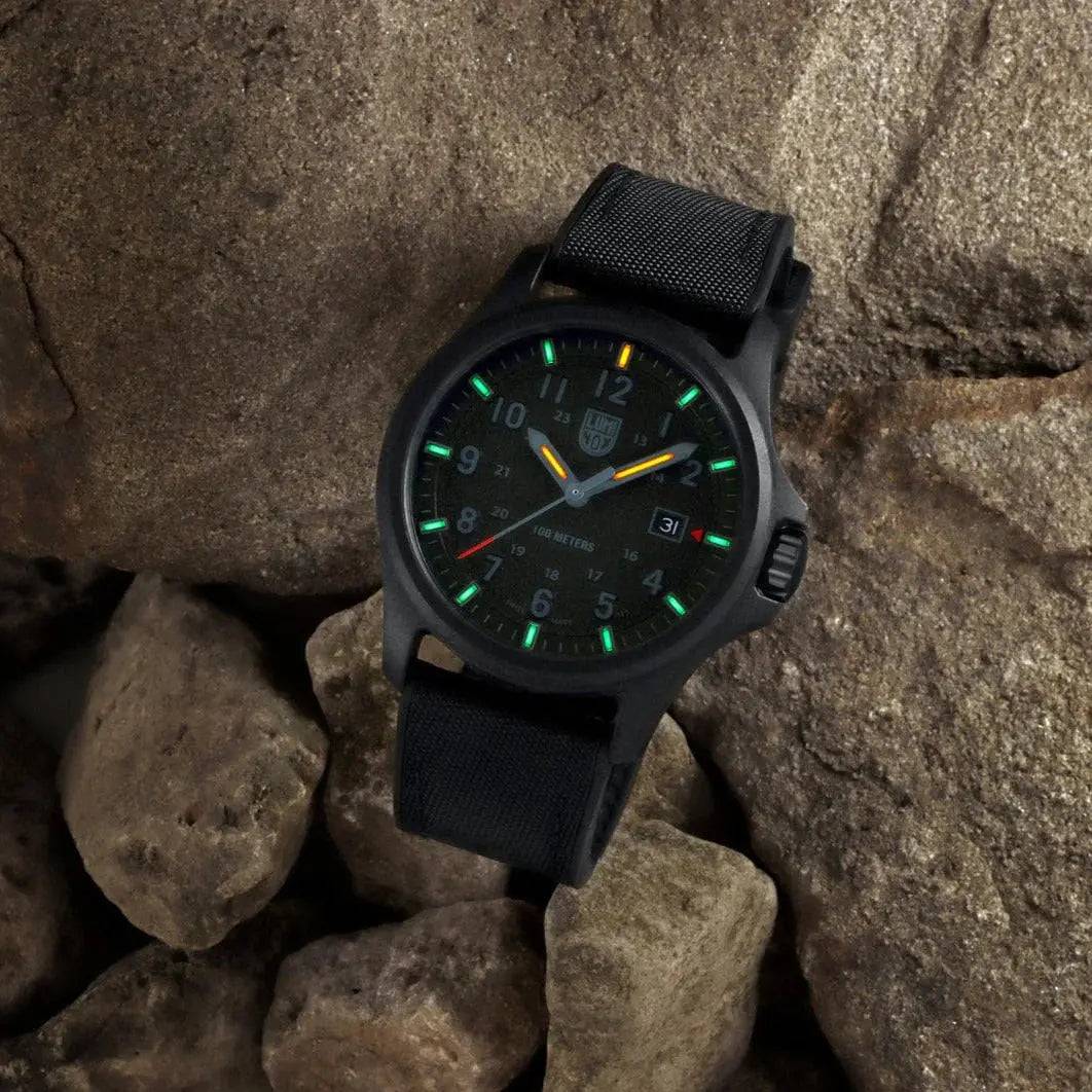 Luminox Atacama Field 1960 Series Watch Black 43mm XL.1961 placed on rocks, glowing in the dark with green and orange luminous markers.
