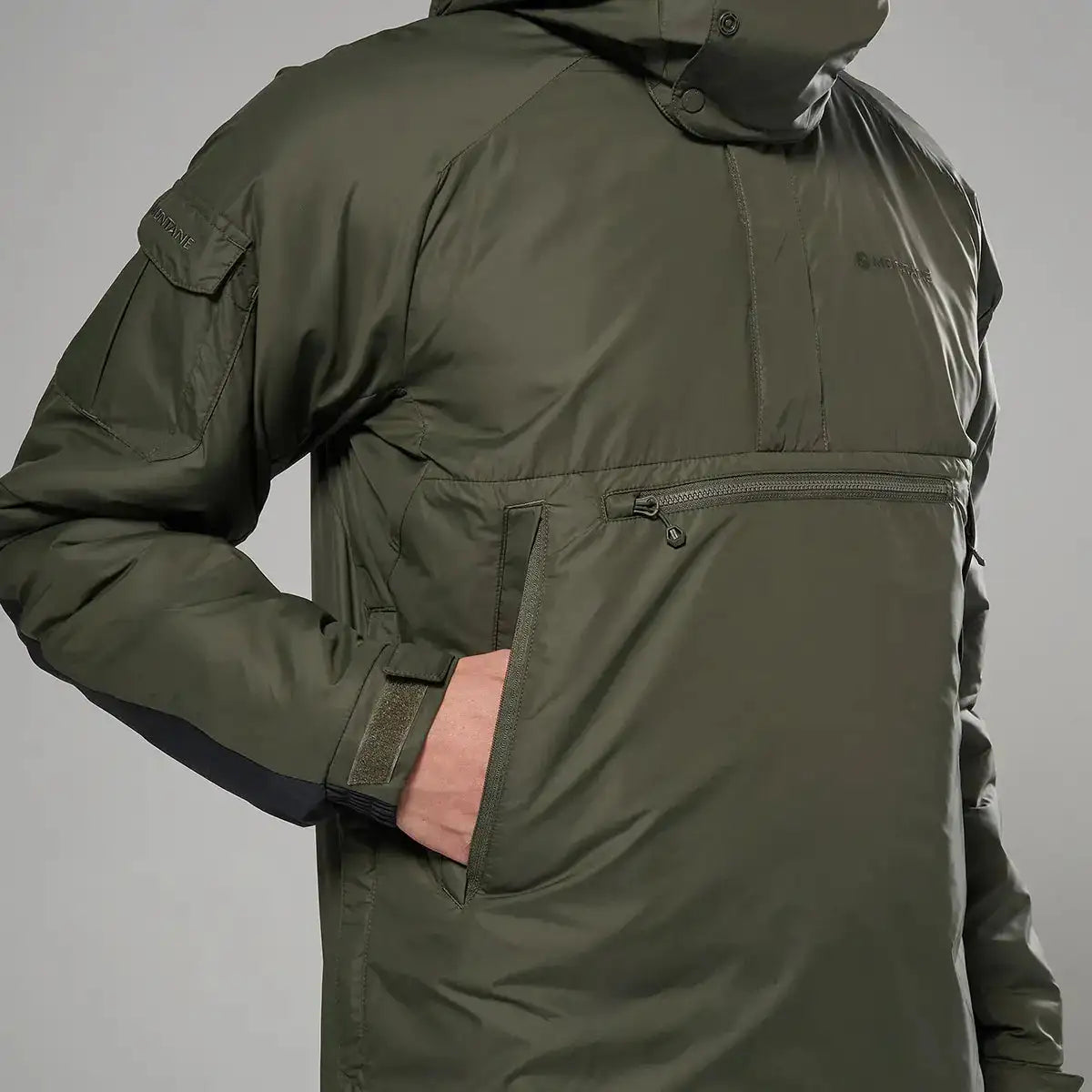 Montane Extreme Smock Insulated Mens jacket in olive with hand in front pocket, showcasing practical storage and warmth, John Bull Clothing. from John Bull Clothing