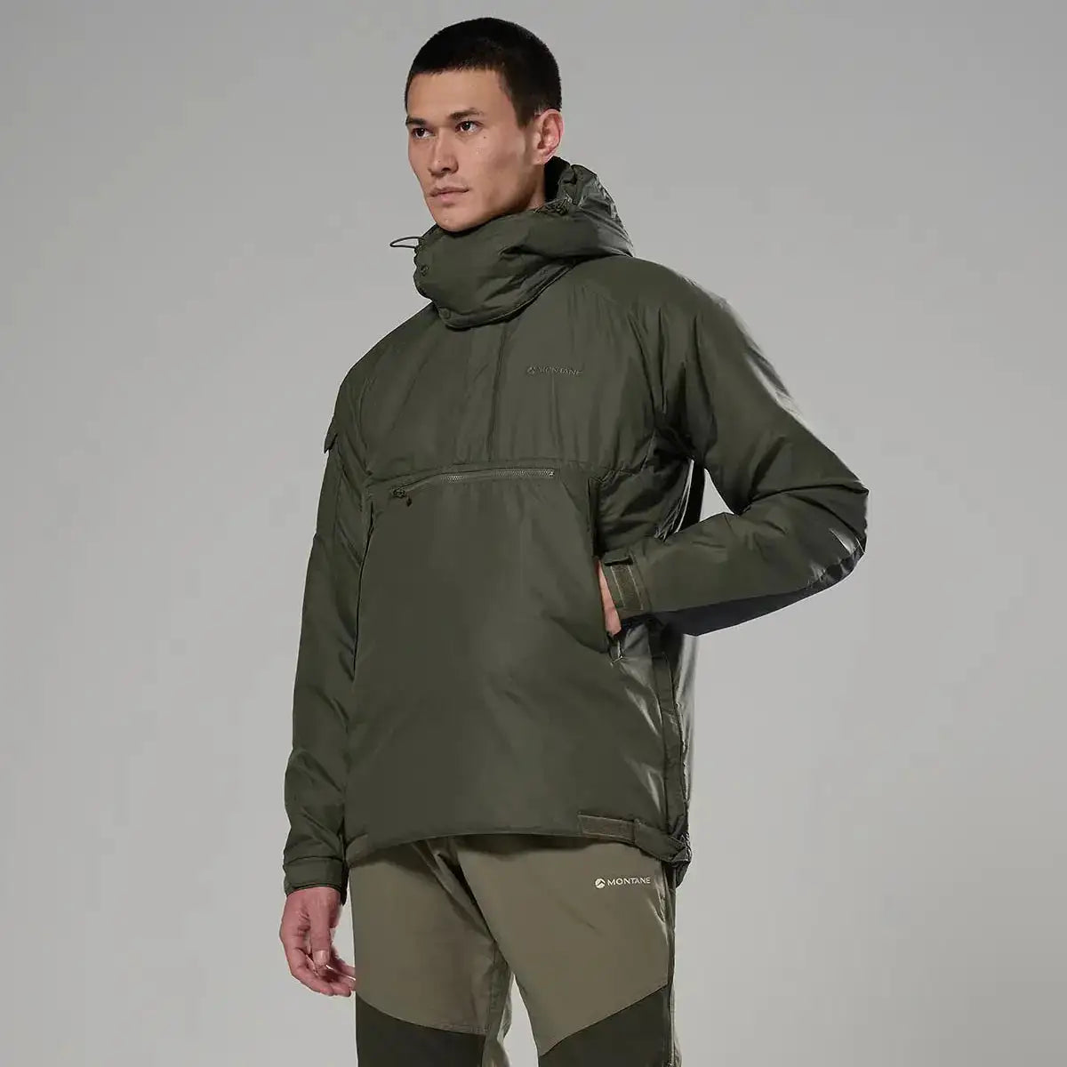 Side view of model in Montane Extreme Smock Insulated Mens olive jacket, showing zippered pocket and articulated fit, from John Bull Clothing. from John Bull Clothing
