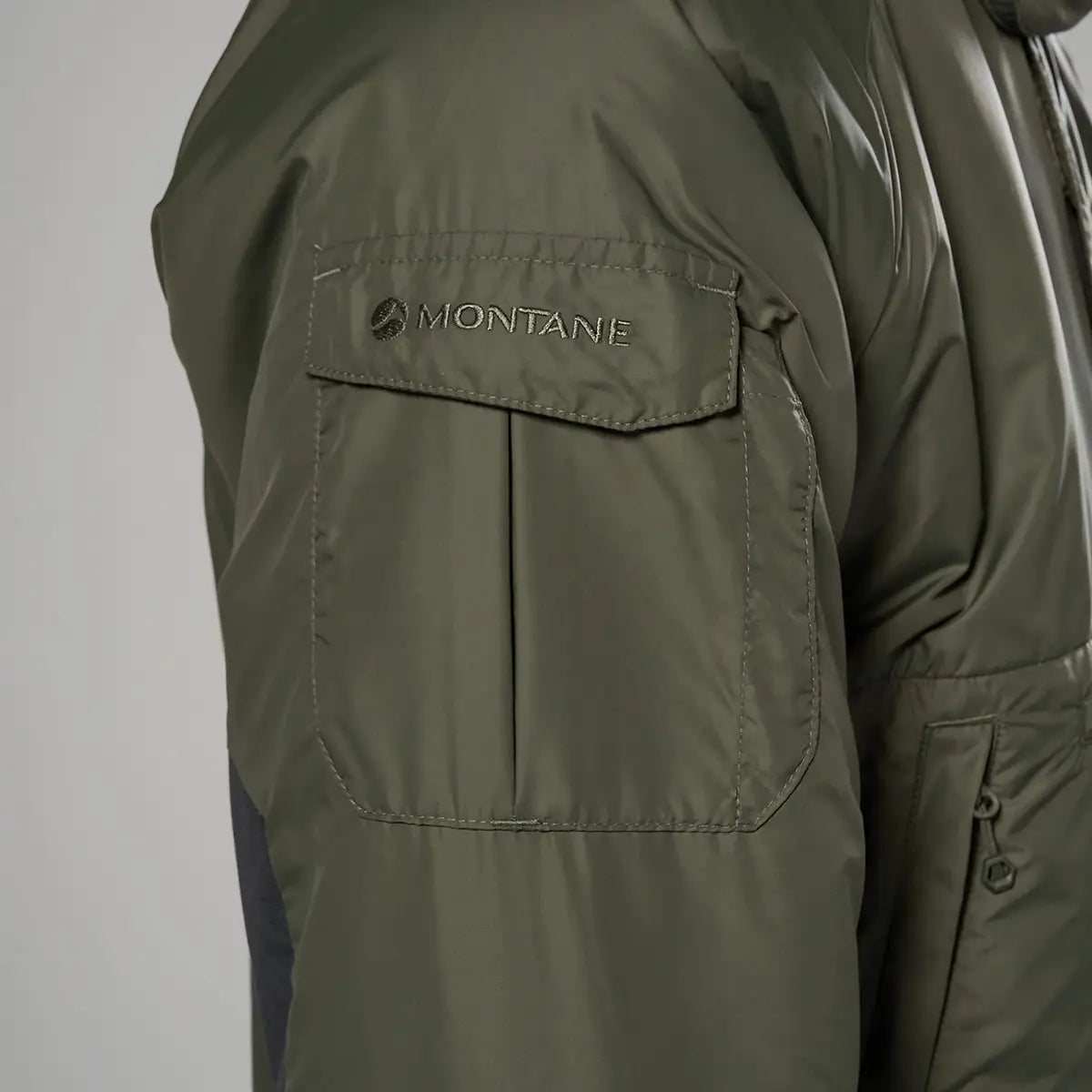 Close-up of Montane logo on sleeve pocket of Extreme Smock Insulated Mens jacket in olive, emphasizing utility and branding, John Bull Clothing.