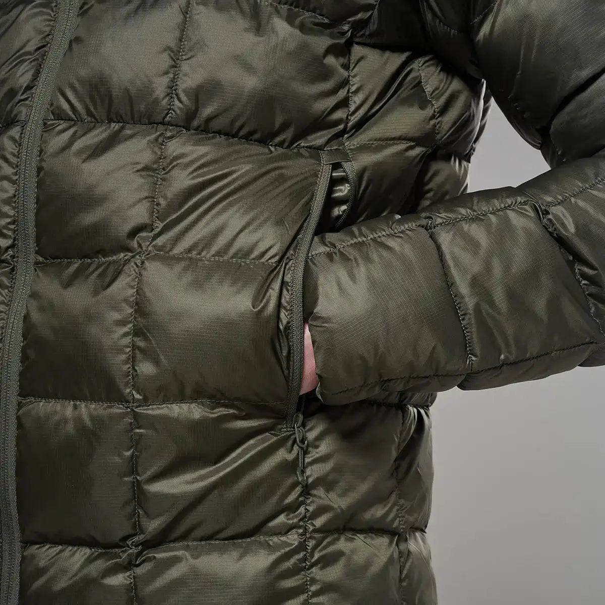 Close-up of a dark green puffer jacket with quilted sections, zipper closure, and a side pocket, designed for outdoor warmth and insulation