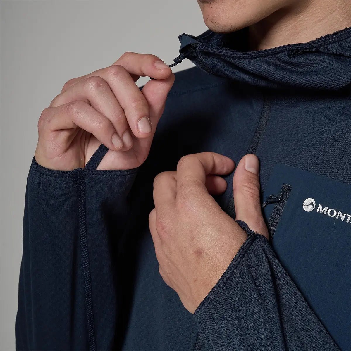 Close-up of a person adjusting the drawstring on a navy Montane Zepher Hooded Fleece Jacket, showcasing the technical outdoor apparel design