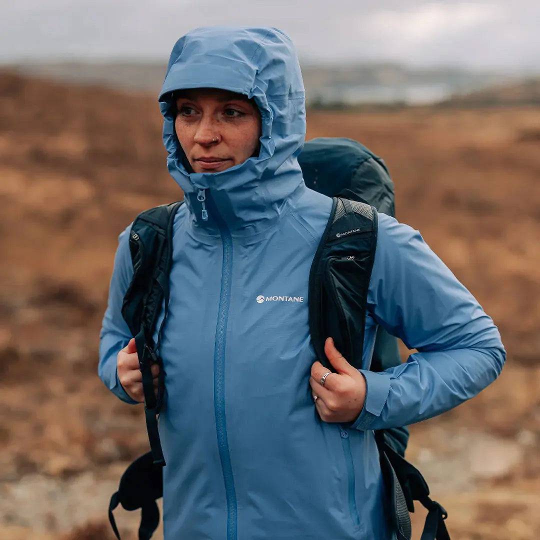 Woman hiking in Montane Women's Cetus Lite Waterproof Jacket in light blue, demonstrating its weather-resistant performance in outdoor conditions.