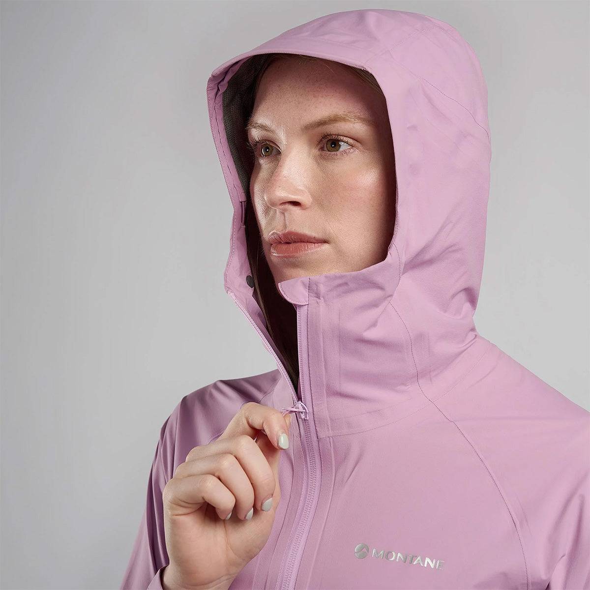 Woman zipping up hooded pink Montane Womans Minimus Lite Waterproof Jacket, highlighting waterproof protection for trail running and hiking.