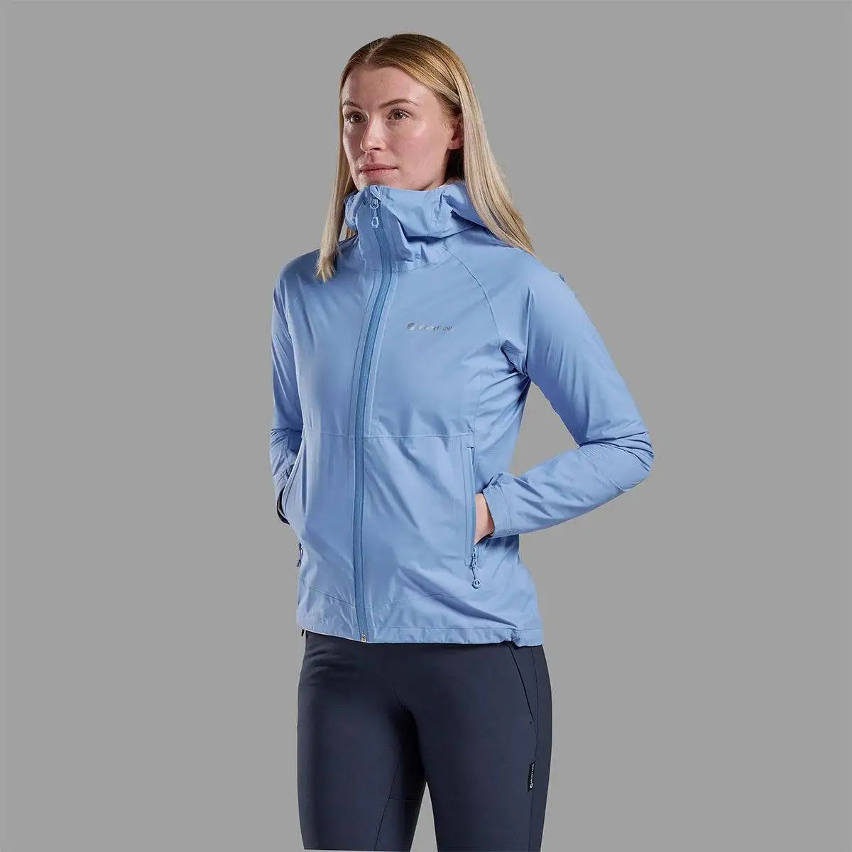 Model wearing sky blue Montane Womans Minimus Lite Waterproof Jacket with hands in pockets, showcasing stylish and functional rain coat for women. from John Bull Clothing