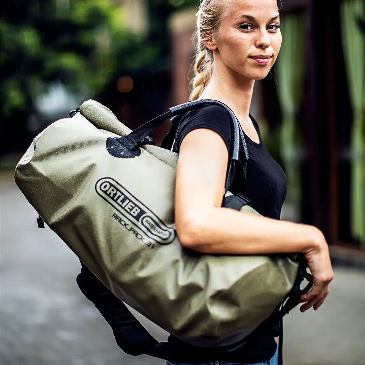 Model carrying olive Ortlieb Rack Pack 31L Waterproof Duffle Bag over shoulder, showcasing its compact size and travel-ready design.