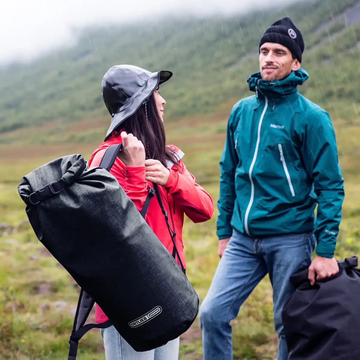 Two hikers in outdoor gear using Ortlieb X-Tremer 35L Carry Bag Black, showcasing its versatility and comfort in wet, rugged environments.