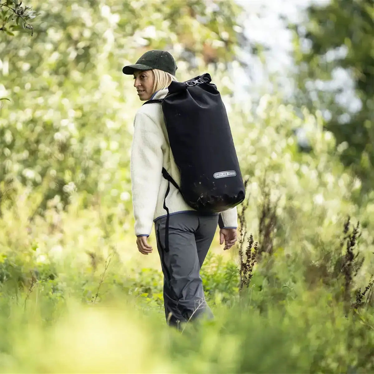 Woman hiking through forest with Ortlieb X-Tremer 35L Carry Bag Black on her back, demonstrating its suitability for outdoor exploration and travel. from John Bull Clothing