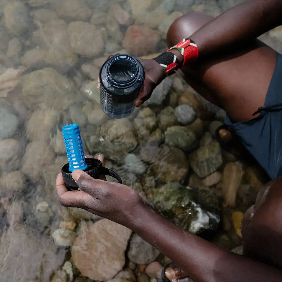 Outdoor enthusiast filling a bottle with Platypus DayCap In Water Bottle Filter from a natural water source for safe drinking.