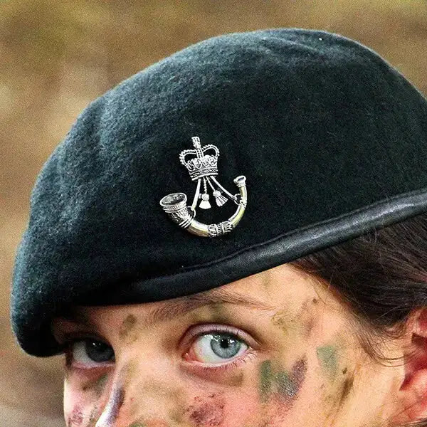 Close-up of a person wearing a Rifles Dark Green wool military beret with a silver Rifles Regiment cap badge with Queens Crown, featuring camouflage face paint.