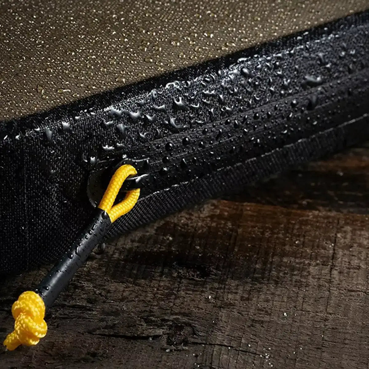 Close-up of a waterproof zippered pouch with water droplets on black fabric and yellow zipper pull, designed for outdoor use