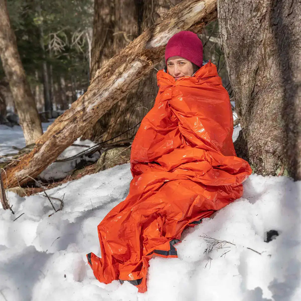 Person wrapped in SOL Emergency Bivvy Bag Shelter with Whistle, sitting in snow for cold-weather survival protection. from John Bull Clothing