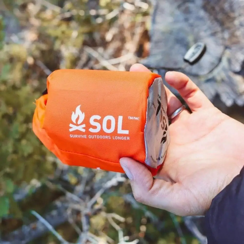 Compact SOL Emergency Bivvy Bag Shelter with Whistle held in hand, showcasing its portable design for field kits.