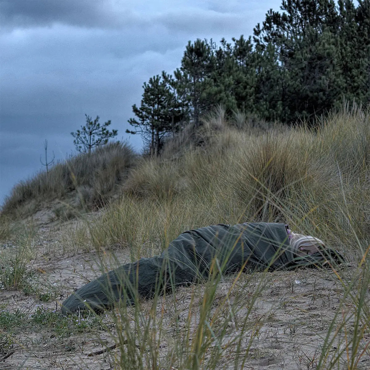 Snugpak Special Forces Waterproof Bivvi Bag WGTE in use on sandy terrain with tall grass, ideal for rugged outdoor camping and survival shelter.