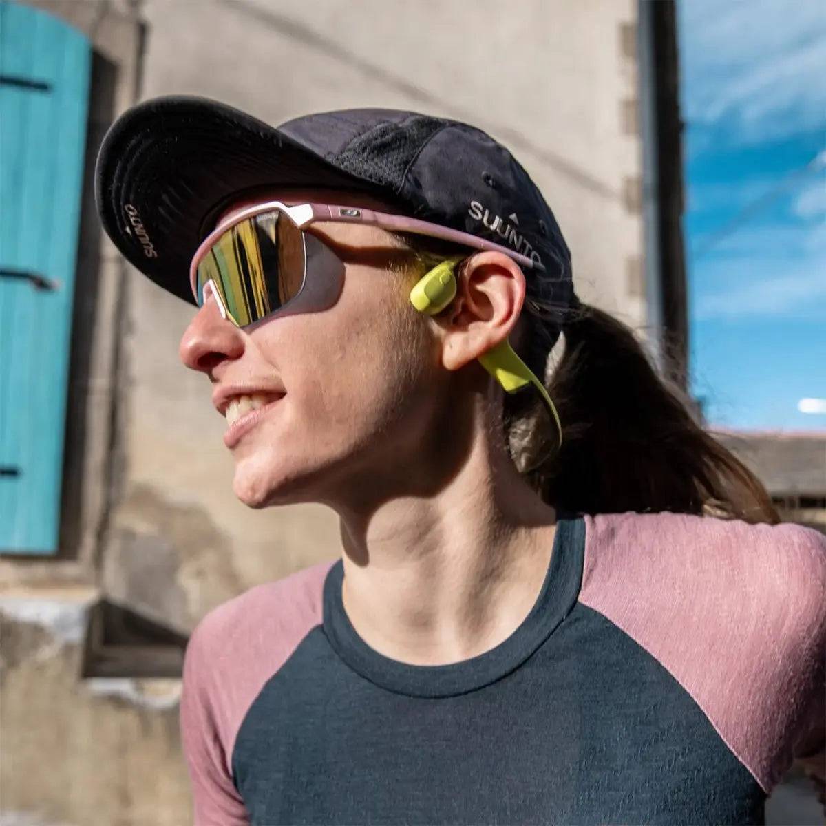 Woman wearing Suunto Sonic Open Ear Bone Headphones in yellow while outdoors, highlighting their lightweight and comfortable design.