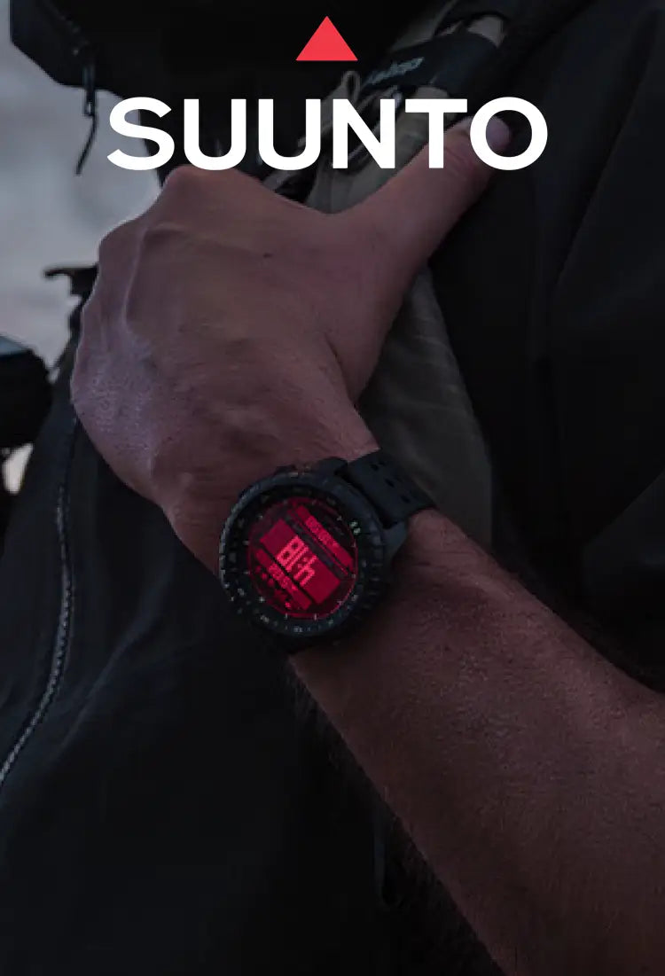 A close-up of a person's arm wearing a Suunto Core 2 digital watch with a black strap and a glowing red display, set against a dark outdoor background with the Suunto logo at the top.