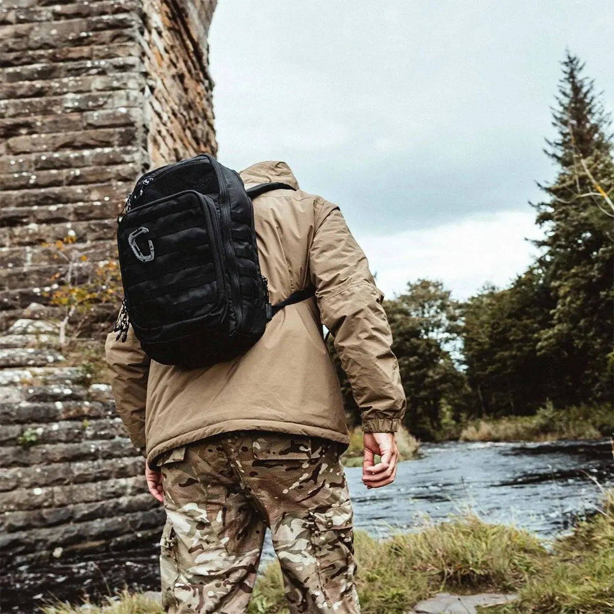 Person wearing Highlander Harrier 25L Clamshell Rucksack in black while trekking outdoors, highlighting its rugged and adventure-ready design.