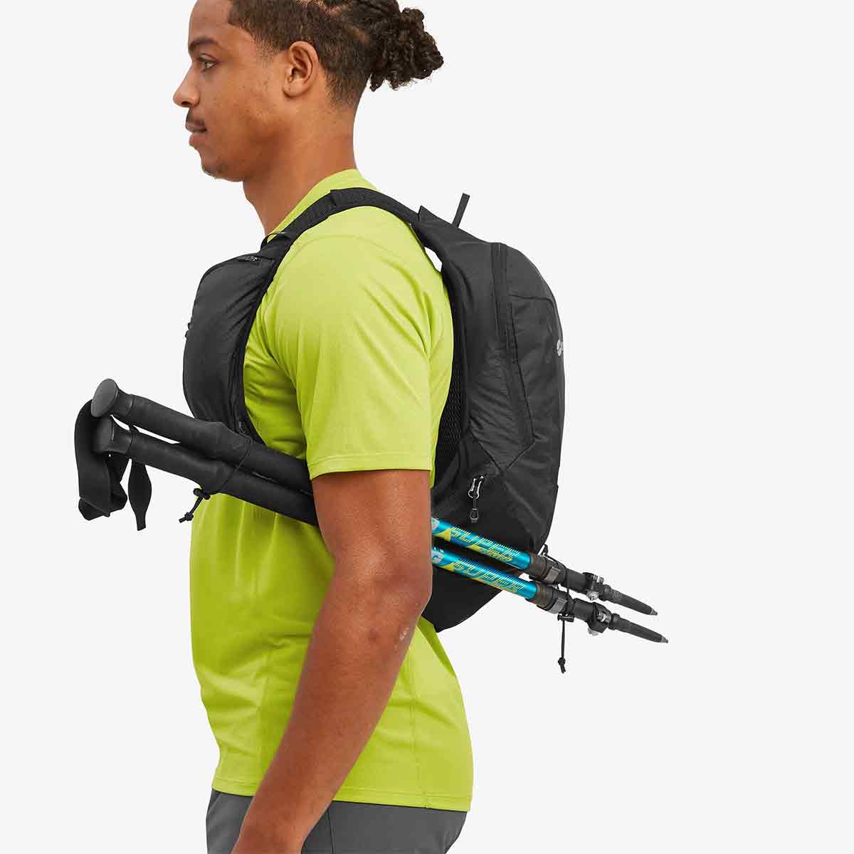 Person wearing the Montane Trailblazer 8L Recycled Backpack with trekking poles attached, showcasing its versatile storage options for outdoor gear and accessories.