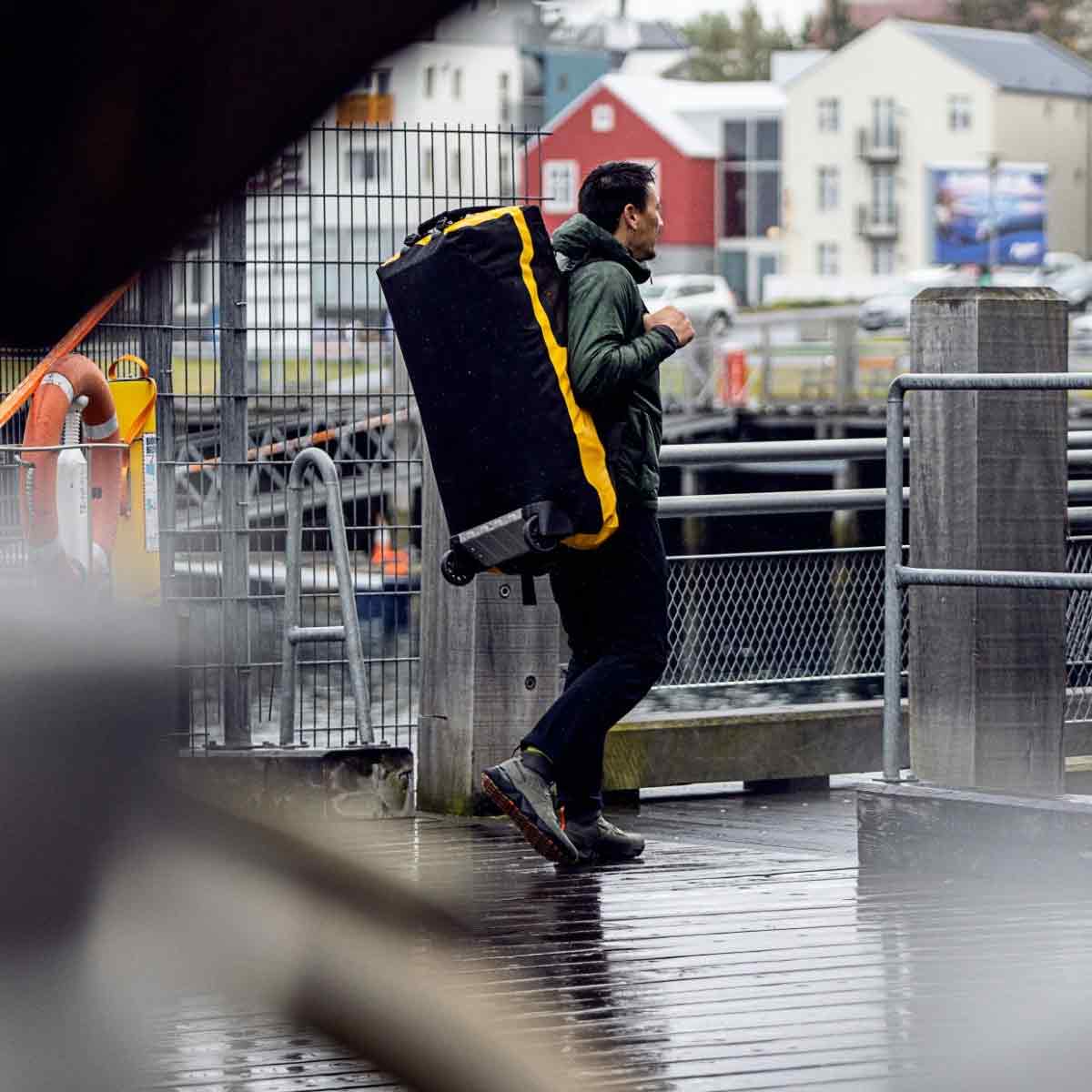 Traveler rolling Ortlieb Duffle RS Travel Bag 140L on a wet dock, showcasing its rugged wheels and waterproof design.