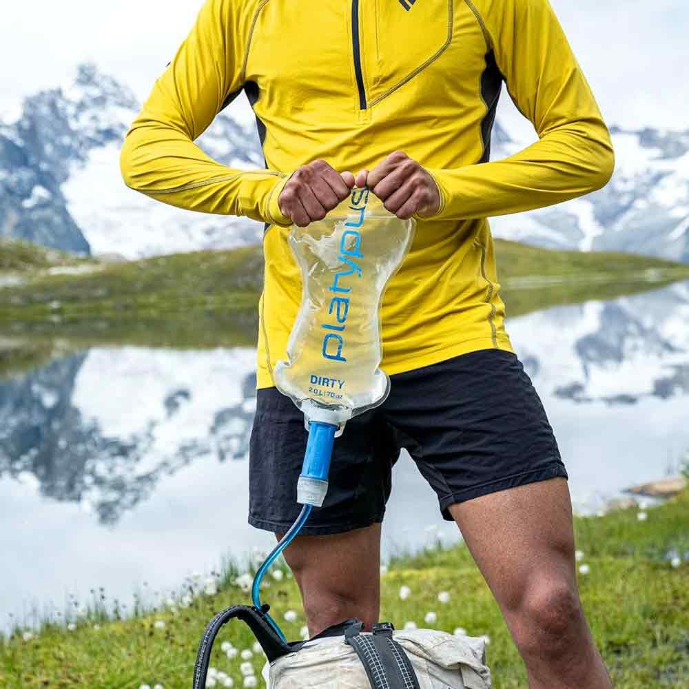 Hiker using the Platypus Quickdraw 2L Filter System in a mountain setting, demonstrating its ease of use for outdoor hydration.