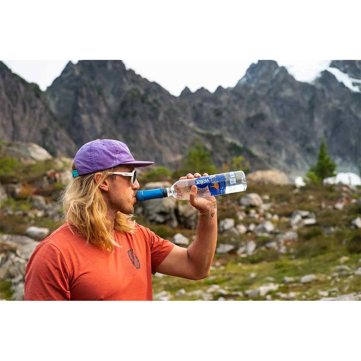 A hiker using the Platypus Quickdraw Water Filter attached to a bottle in a mountain setting. Ensures safe drinking water during outdoor excursions.