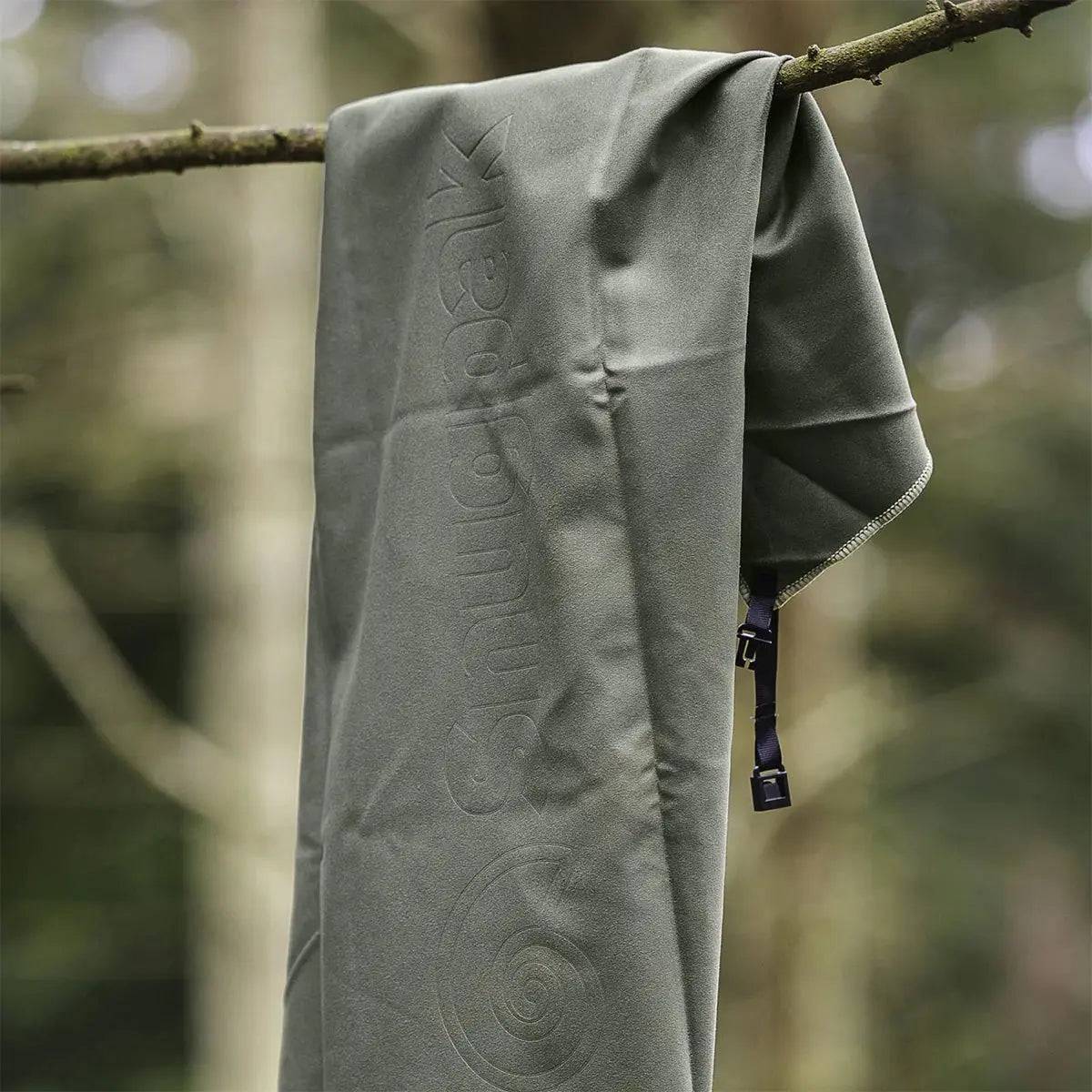 Snugpak Head to Toe Travel Towel in Olive hanging on a tree branch. Lightweight, absorbent, and perfect for camping or hiking trips.