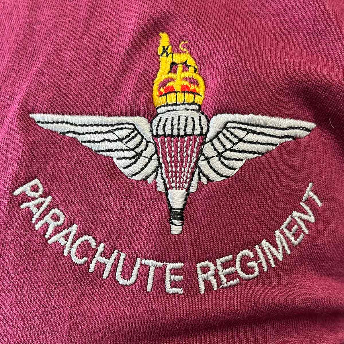 Close-up of embroidered Parachute Regiment badge and text on maroon cotton t-shirt, highlighting design quality and detail.