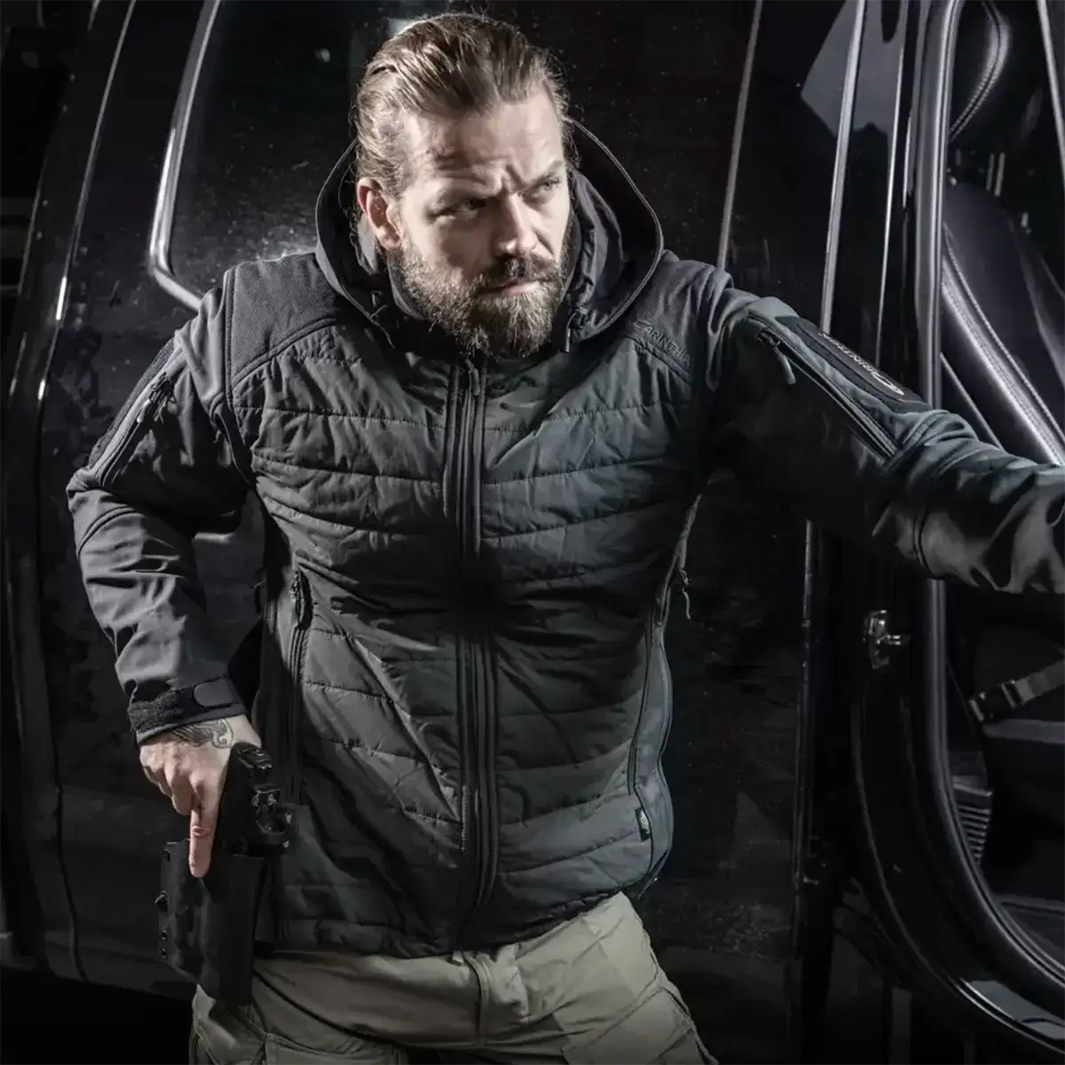 Man wearing the navy blue Carinthia G-Loft ISG PRO jacket, standing next to a vehicle, demonstrating its fit and tactical style for outdoor activities.  from  John Bull Clothing 
