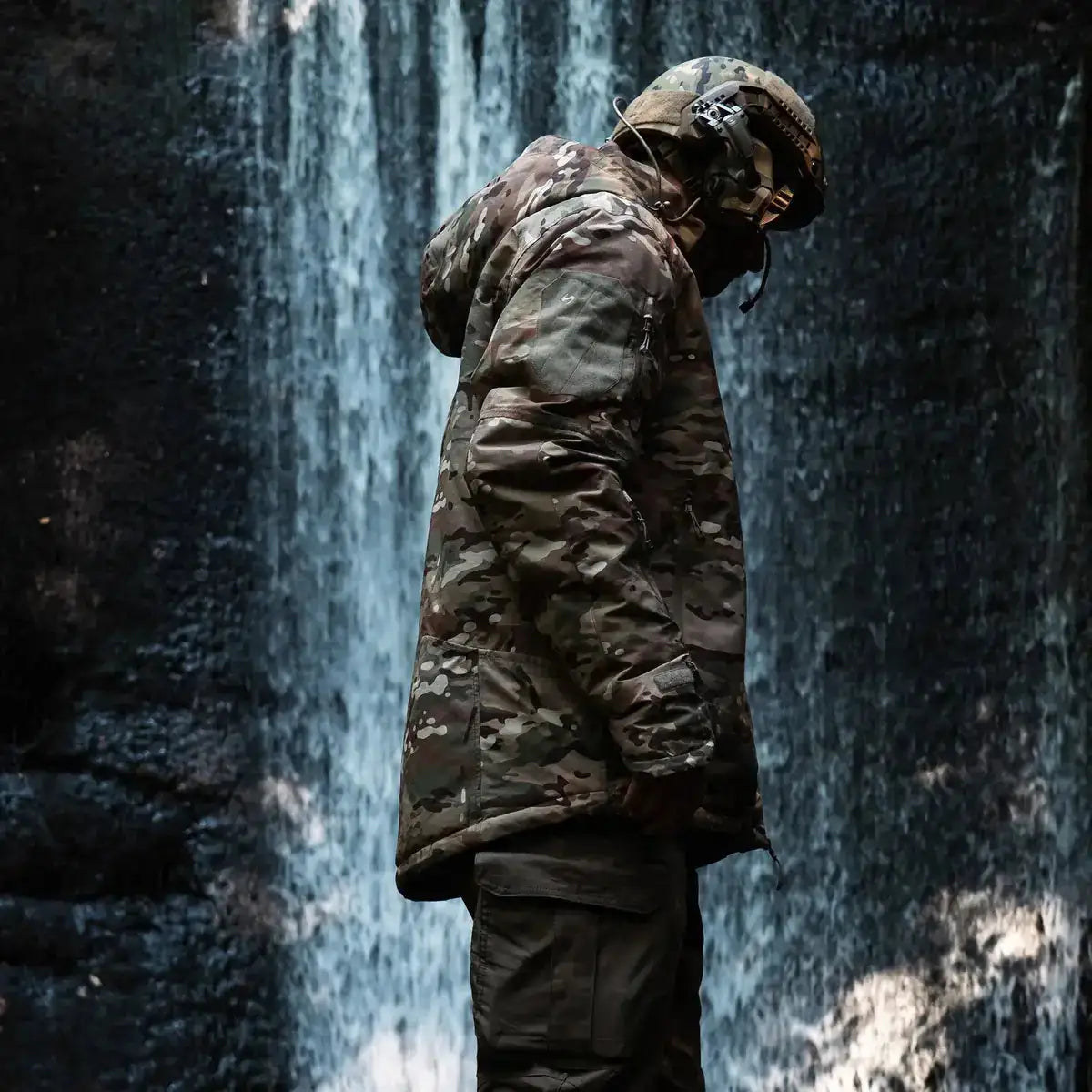 Person wearing Stoirm Mission Primaloft Waterproof Jacket Multicam in outdoor setting near waterfall, demonstrating rugged tactical use.  from  John Bull Clothing 