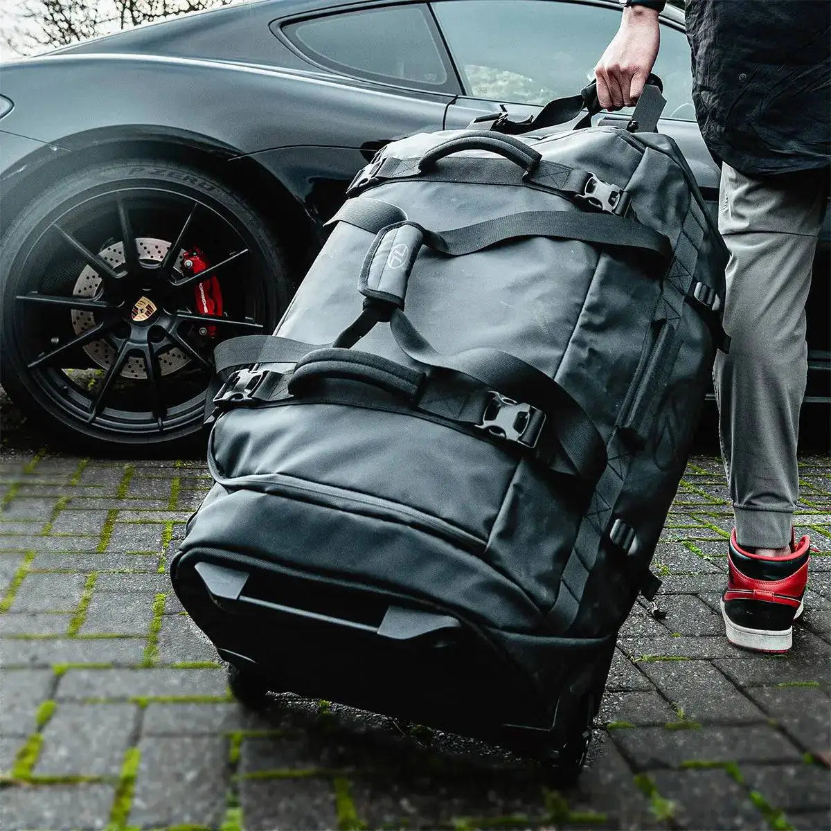 Person pulling the Highlander The Trailer 100 Litre Duffel Bag Black on wheels, highlighting its travel-friendly design and large storage capacity.  from  John Bull Clothing 