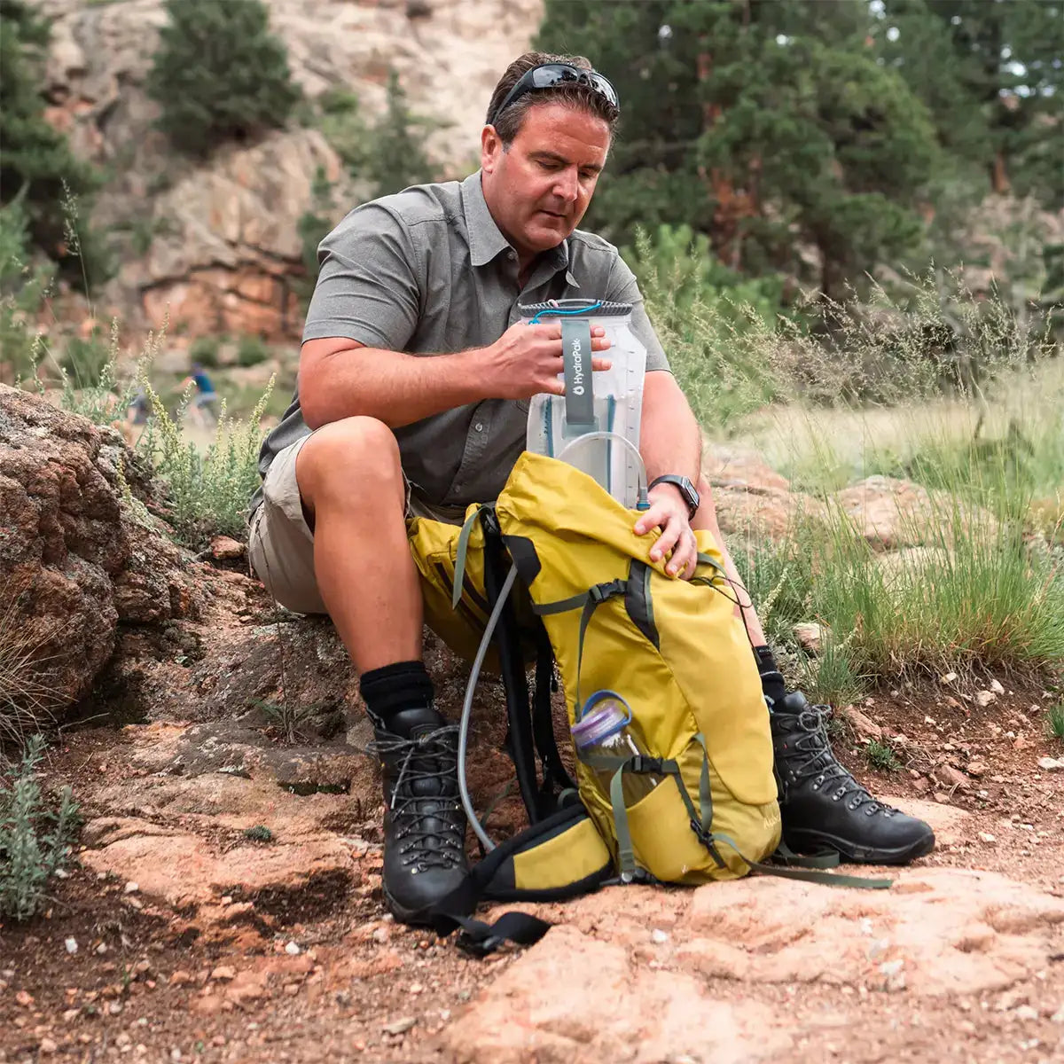 Man placing HydraPak Contour Clear Water Reservoir into hiking backpack, showcasing its compact and portable design for outdoor use.  from  John Bull Clothing 