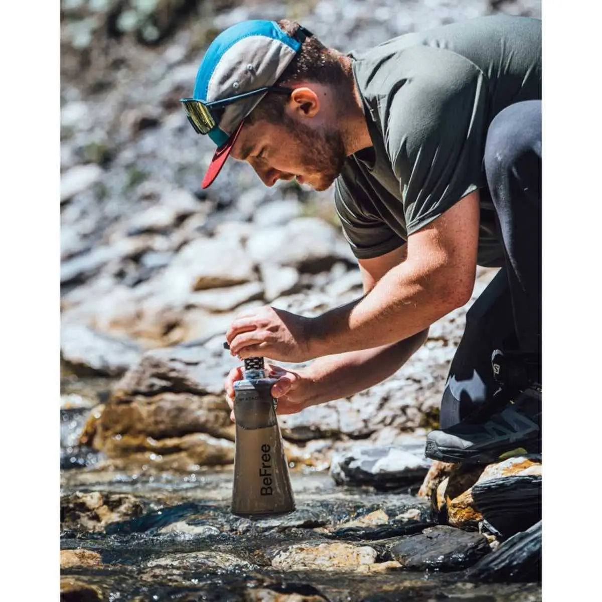 Man using Tactical Black Katadyn BeFree AC Water Filter Bottle 1.0L to filter water from a river, ideal for camping and hiking.  from  John Bull Clothing 