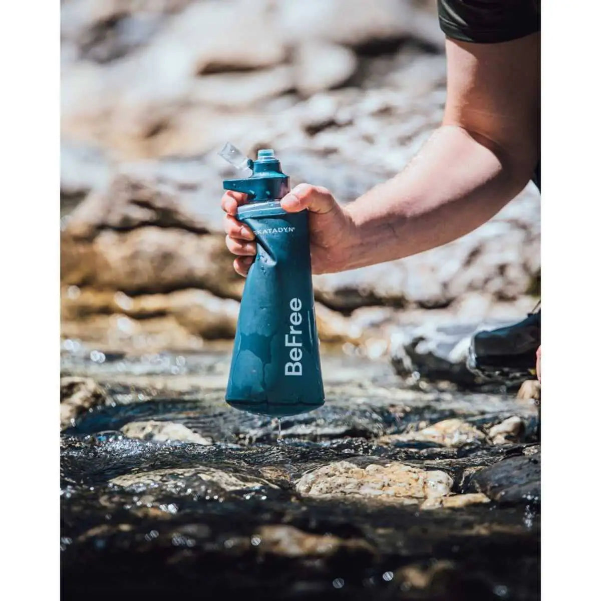 Person collecting stream water using Katadyn BeFree AC Water Filter Bottle 1.0L in Slate Blue, perfect for outdoor hydration.  from  John Bull Clothing 