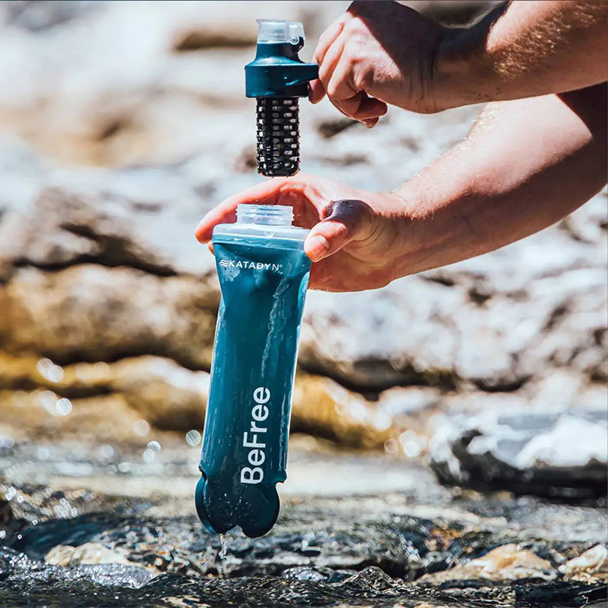 Katadyn BeFree AC Water Filter Bottle 500ml Slate Blue being filled from a stream, demonstrating its use in outdoor water purification.  from  John Bull Clothing 