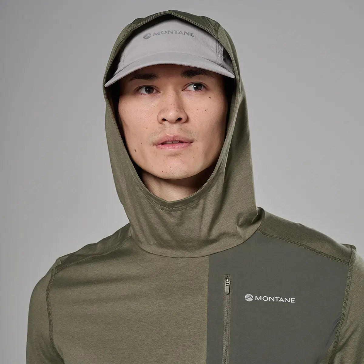 Close-up of male model's face wearing light gray cap and hooded jacket with Montane logo, showing the hood and high collar