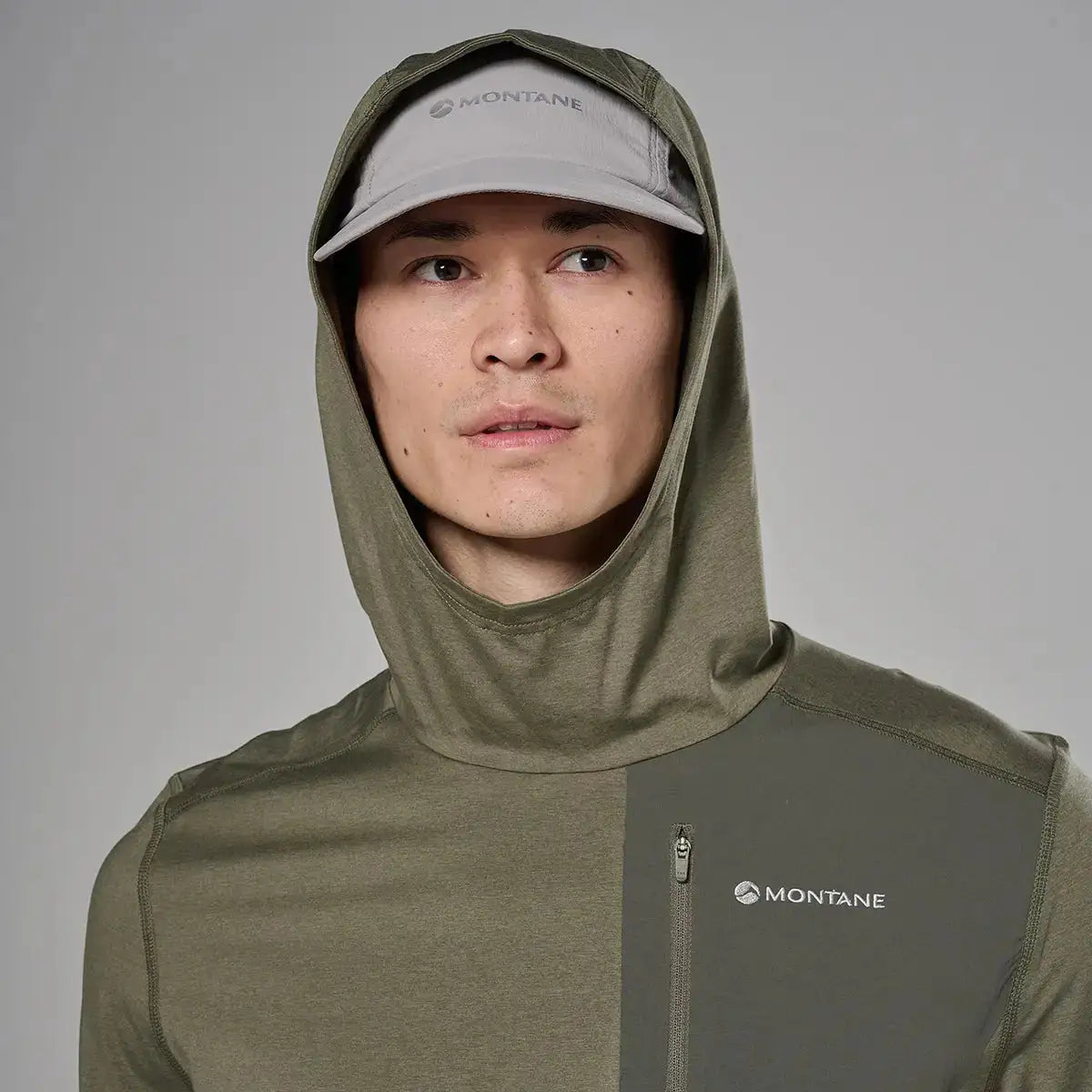 Close-up of male model's face wearing light gray cap and hooded jacket with Montane logo, showing the hood and high collar