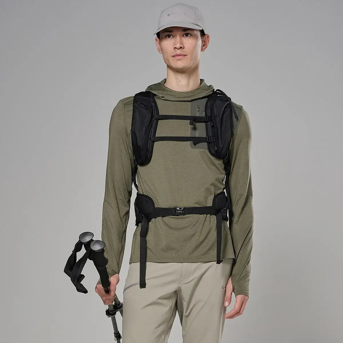 Male model wearing olive green hooded outdoor jacket with long sleeves, adjustable cuffs, and a front zipper, holding trekking poles