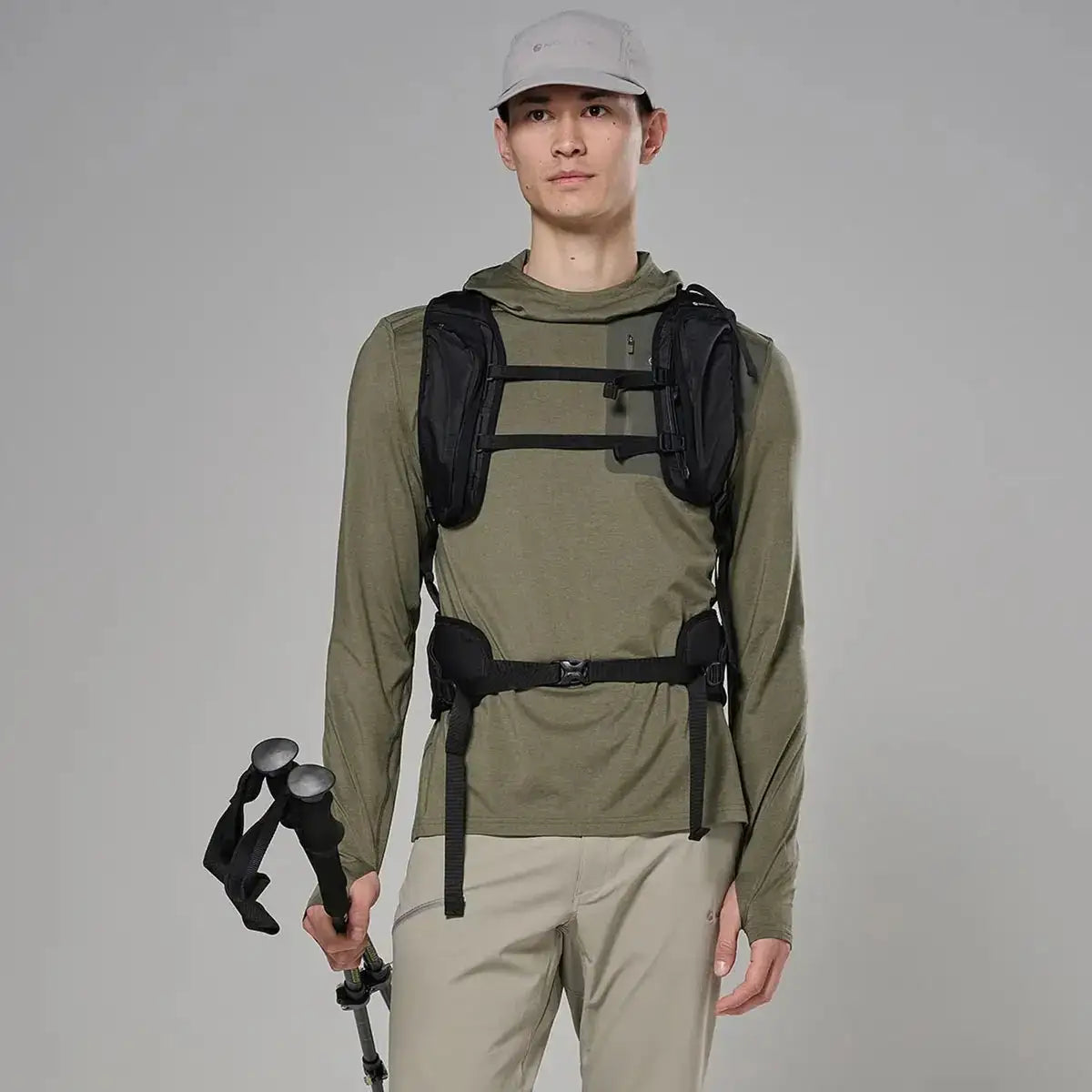 Male model wearing olive green hooded outdoor jacket with long sleeves, adjustable cuffs, and a front zipper, holding trekking poles