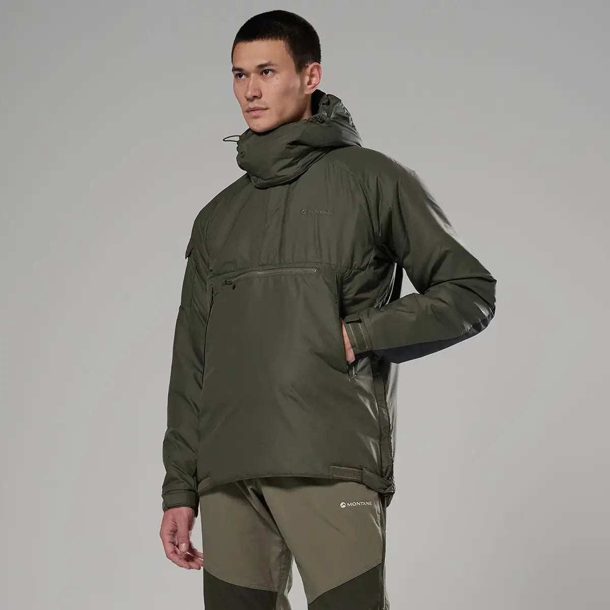 Side view of model in Montane Extreme Smock Insulated Mens olive jacket, showing zippered pocket and articulated fit, from John Bull Clothing.