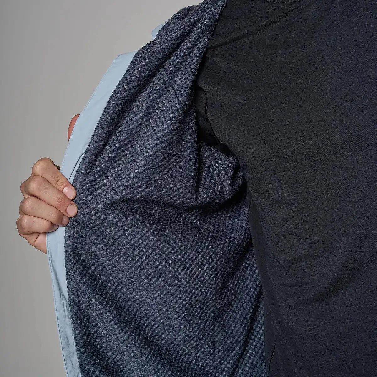 Close-up of a person holding open a navy blue softshell jacket with textured fabric, black inner layer, and light blue lining, suitable for outdoor wear.