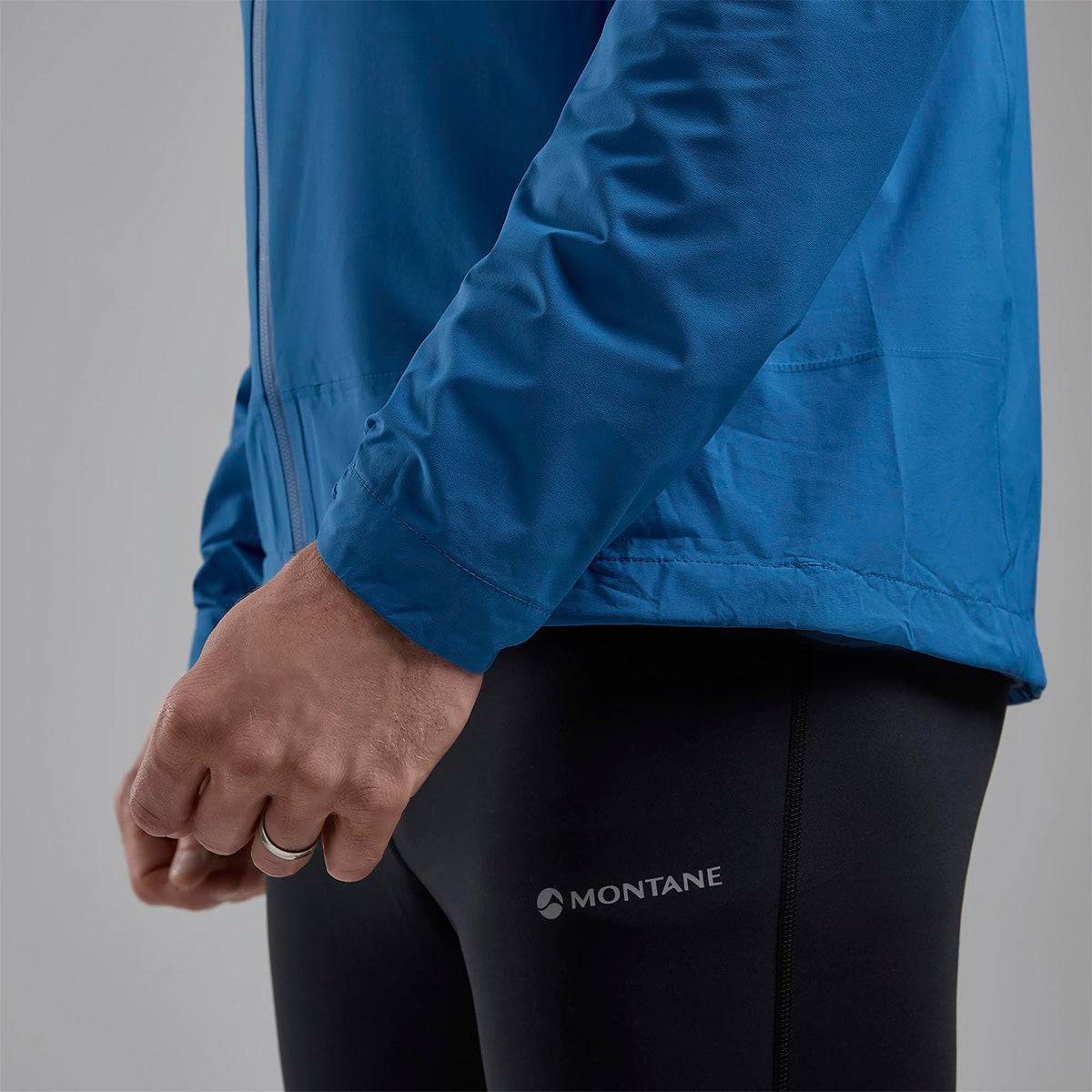Close-up of Montane branding on blue Minimus Lite Waterproof Jacket, paired with black leggings for outdoor performance wear.