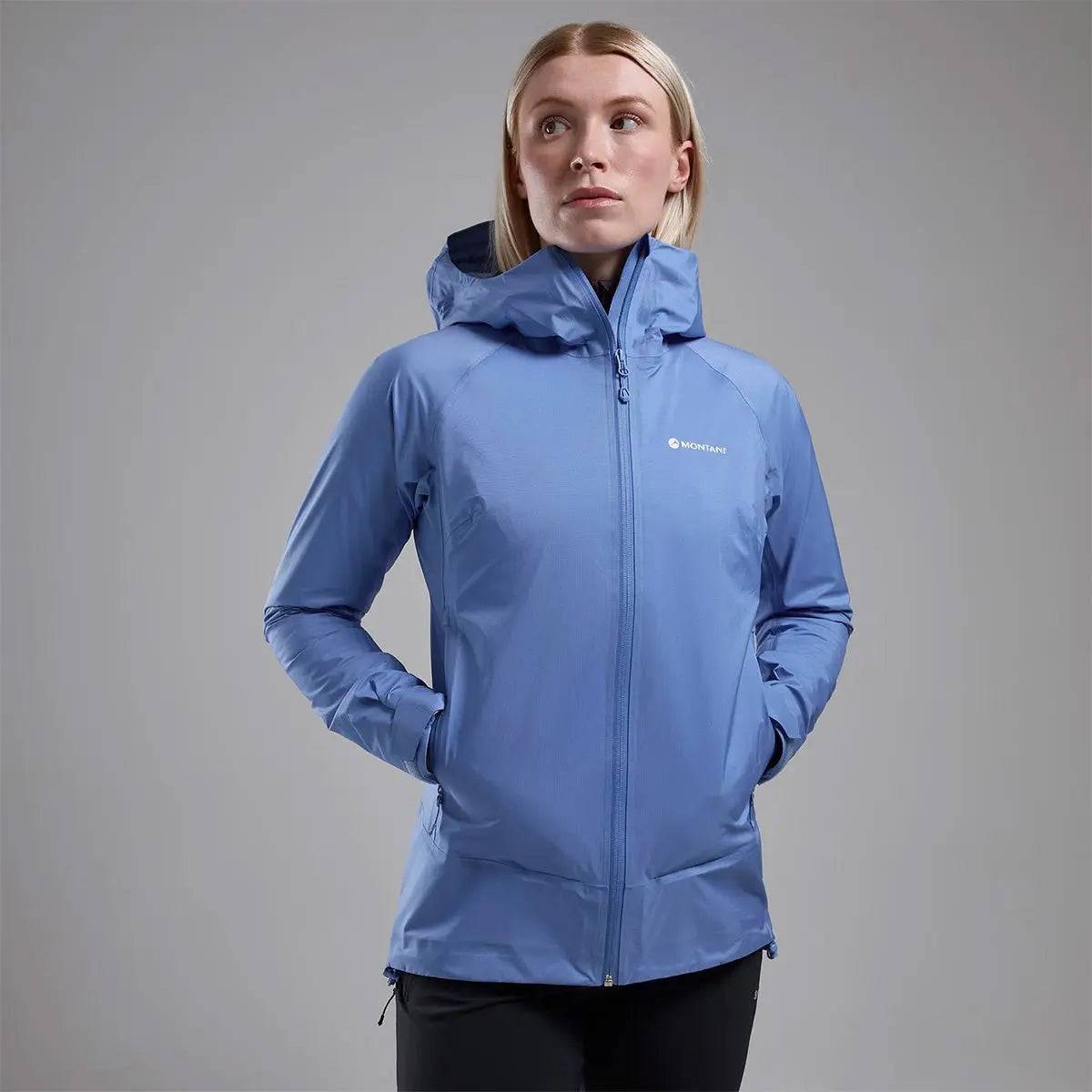 Model wearing Montane Women's Cetus Lite Waterproof Jacket in light blue, featuring a fitted hood and zippered pockets for convenience.